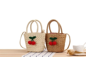 Detail of hand-woven straw bags with 3D crochet cherry accents on wooden background