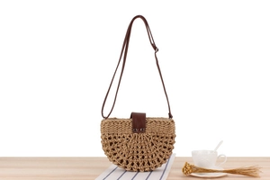Detail of a semi-circular woven straw bag with dark brown leather strap on a table