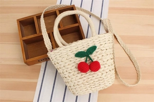 Close-up of beige woven straw bag with red crochet cherries and natural fiber texture