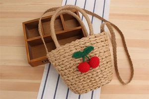 Close-up of woven straw handbag featuring cute knitted cherry details on wooden surface