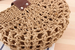 Detail of hand-woven straw shoulder bag with dark brown leather flap and silver rivets