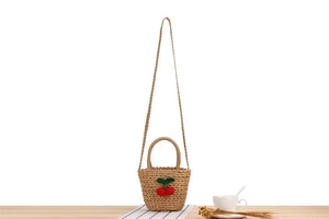 Detail of woven straw bag featuring handmade crochet cherry decor and wood handles