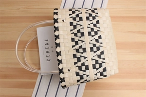 Detail of woven checkerboard tote bag with transparent handles on a wooden table