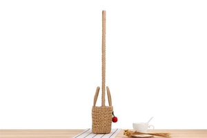 Detail of hand-woven straw bag with cute rabbit ears and red cherry charm on wood table