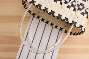 Detail of handwoven black and white checkered tote bag with clear tube handles on wood