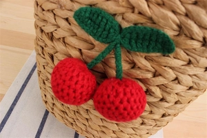Macro detail of red crochet cherries with green leaves on a straw woven beach bag