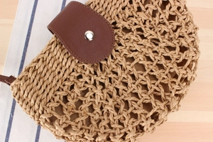 Close-up of woven straw bag with dark brown leather flap and silver metal snap closure