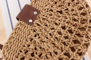 Detail view of woven straw shoulder bag featuring a brown leather clasp and metal rivets
