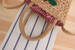 Close-up of woven straw bag with red striped lining and green leaf knit detail