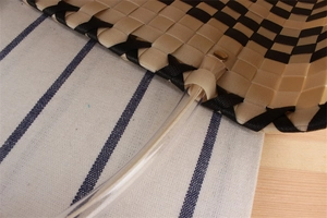 Detail of woven checkerboard bag with clear tube handle and metal rivet reinforcement