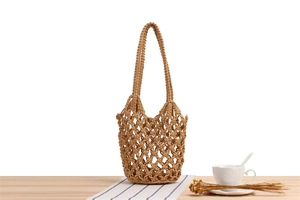 Detail of crochet beach tote bag with hollow mesh design on light wooden table