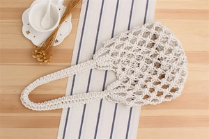 Detail of the woven texture and mesh pattern of a beige crochet beach bag on a wooden surface