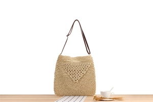 Dettaglio di una borsa a tracolla in paglia intrecciata beige su un tavolo di legno