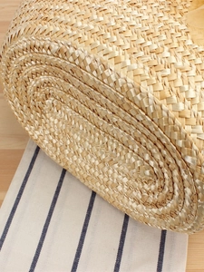 Handwoven straw beach bag with reinforced spiral base on a rustic linen background