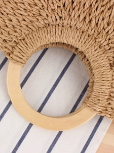 Handmade woven straw bag with circular wooden handles and natural fiber texture for beach style
