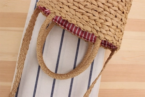 Détail du sac en paille tissée avec doublure rayée rouge et blanc et texture naturelle