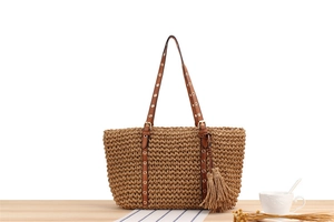 Detail of woven straw tote bag with brown leather handles and decorative metal rivets