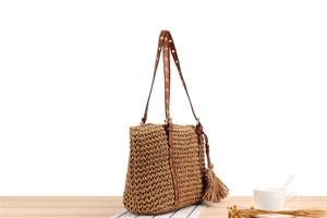 Close-up of handwoven straw tote bag with brown leather straps and stylish tassel detail
