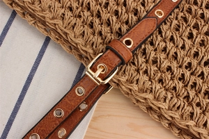 Detail of adjustable brown leather strap with gold eyelets on woven straw beach tote bag