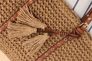Detailed macro of hand-woven straw shoulder bag featuring fringe tassels and metal eyelets