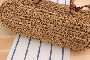 Close-up of the woven texture and leather handle details on this straw beach shoulder bag