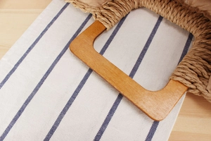 Gros plan d'un sac de plage tissé avec des poignées rectangulaires en bois et doublure