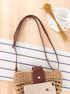 Minimalist handmade woven straw shoulder bag with leather strap on a rustic table