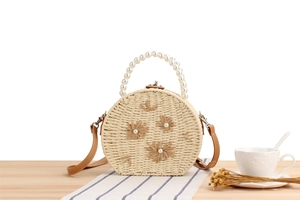 Détail du sac rond en paille avec anse en perles, fleurs et bandoulière en cuir brun