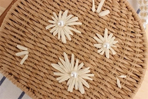 Détail macro d'un sac rond en paille tissé main avec fleurs de marguerite brodées et perles