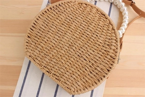 Détail d'un sac rond tressé avec poignée en perles blanches et bandoulière en cuir marron