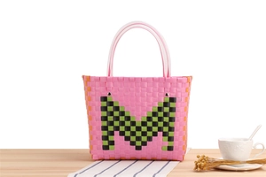 Detail of pink woven basket bag with green checkered M logo on a rustic wooden table