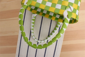 Detail einer grün-gelb karierten handgewebten Mini-Korb-Tasche aus Nylon auf Holzfläche