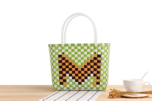Detail of handwoven green and white checkered tote bag with orange M pattern on table