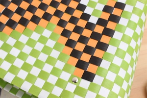 Close-up of woven basket bag showing green, white and orange checkerboard pattern with rivet