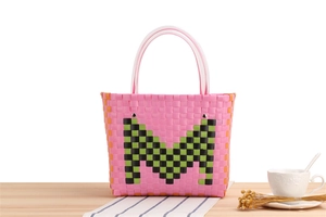 Detail of pink woven tote bag with green M letter and transparent plastic handle