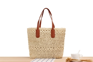Detailed view of hollow woven straw tote bag with brown leather handles on wooden table