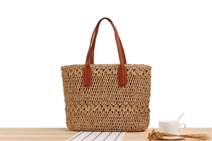 Detail view of a woven straw tote bag with brown leather handles on a wood surface