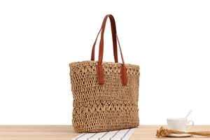 Macro view of woven straw tote bag texture and brown leather handle on a table