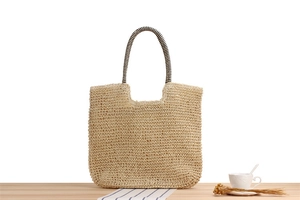 Detail of beige handwoven straw tote bag with black and white striped handles on wood