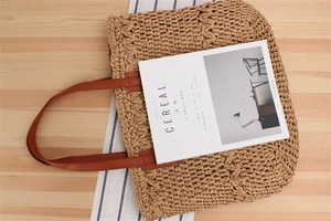 Detailed top view of a woven straw tote bag on a wooden background with a magazine
