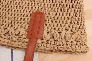 Close-up of woven straw bag detail with brown leather strap and neat stitching