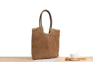 Detail of hand-woven straw tote bag with striped handles on a wooden table setup
