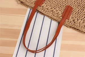 Close-up of brown leather handles and woven paper rope texture on a summer beach bag