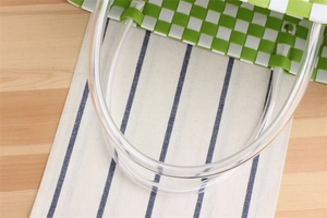 Close-up of green and white woven basket bag with clear tube handles and metal rivets