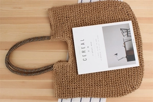 Top view of a handmade straw beach bag with striped handles on a wooden table