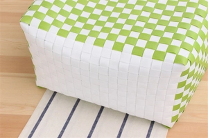Top view of hand-woven checkerboard basket in green and white on a striped mat