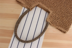 Detail of hand-woven straw tote bag with spiral handle on wooden table and striped cloth