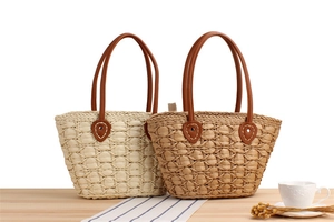 Detailed view of woven straw tote bag with brown leather handles and premium stitching