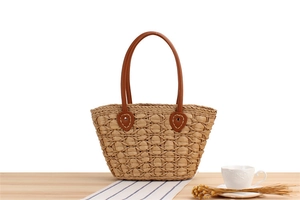 Detailed close-up of woven straw tote bag with brown leather handles on a wooden table