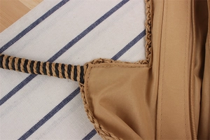 Detail of dark brown hand-woven straw bag showing secure zipper and dual-tone handle